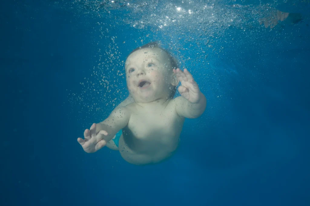 Bébé garçon nageant sous l'eau. Il a les yeux grands ouverts et il a l'air de rire