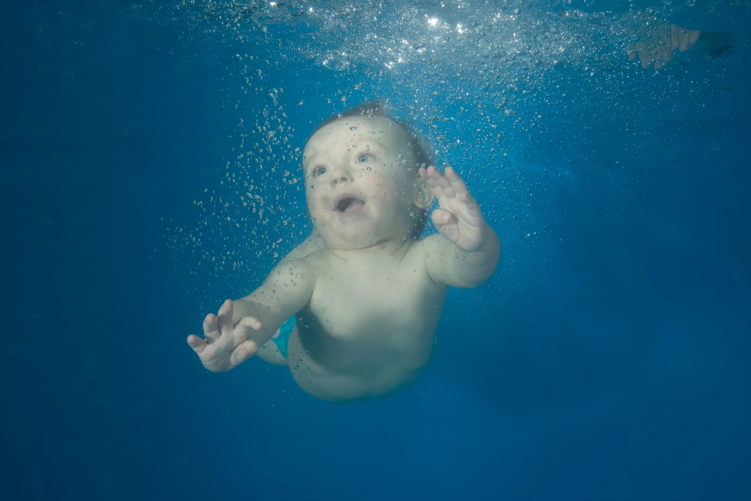 Bébé garçon nageant sous l'eau. Il a les yeux grands ouverts et il a l'air de rire