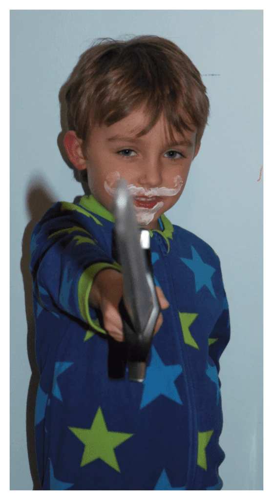 Junge mit krausem Schnurrbart und Spitzbart, der mit Ekzemschutzcreme aufgemalt ist. Er schwingt ein Spielzeugschwert in der Position 'Wache'. Definitiv eine lustige Schlafenszeit-Routine!