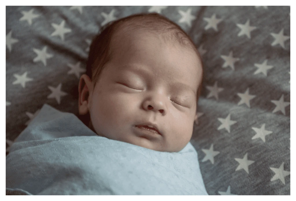 Bébé endormi dans une pièce sombre. Le bébé est emmailloté afin qu'il ne puisse pas utiliser ses mains pour gratter son eczéma.