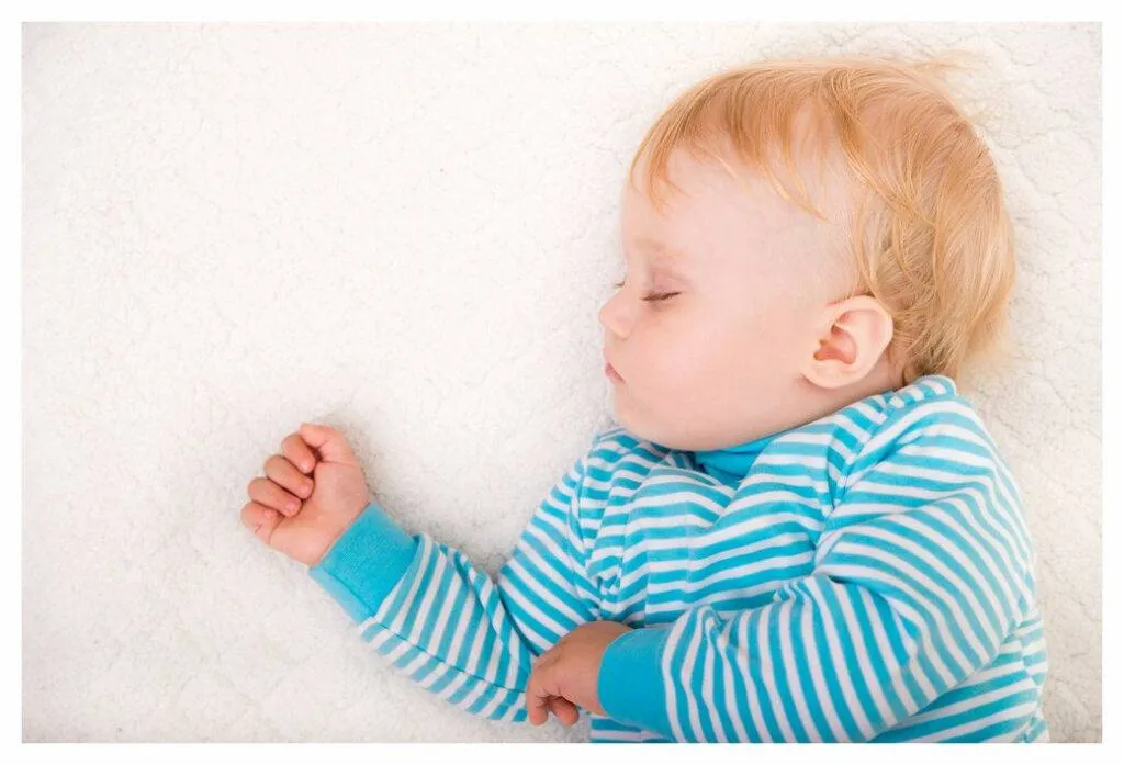 Jeune enfant en haut rayé bleu et blanc dormant sur le dos. Il dort profondément et semble rêver de boxe ! 